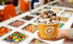 a person holding up an orange cup filled with ice cream and toppings on top of it