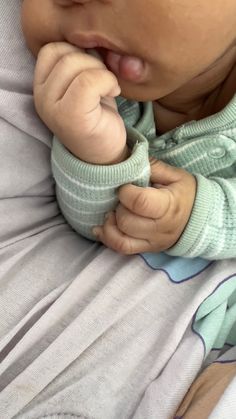 a close up of a baby laying in a bed with its hand on his mouth