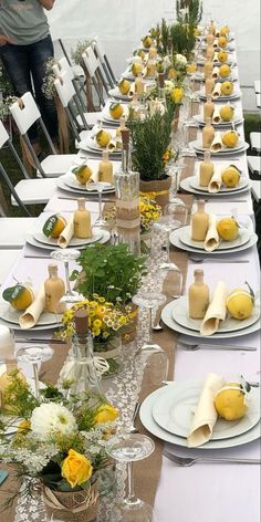 a long table is set with white plates and yellow flowers