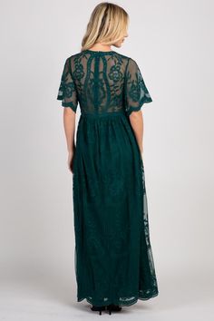 a woman wearing a dark green dress with sheer sleeves and an intricate lace overlay