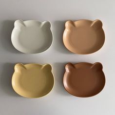 four different colored cat shaped plates on a white surface with one brown, one beige and one black