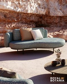 a couch and coffee table sitting in the middle of a desert area with large rocks behind it