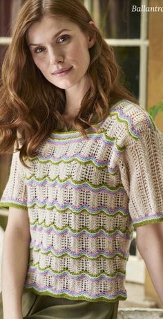 a woman standing in front of a window wearing a knitted shirt and green pants