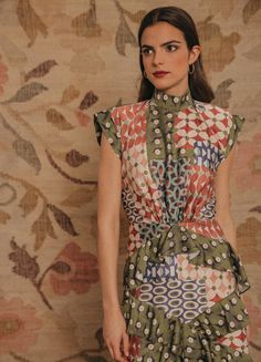 a woman standing in front of a wall wearing a green and red dress with circles on it