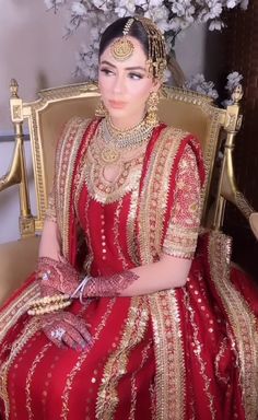 a woman in a red and gold dress sitting on a chair with flowers behind her