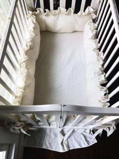 a white crib with ruffles and sheets on it