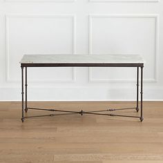 a white marble top coffee table with black iron legs on a wood floor in front of a white paneled wall