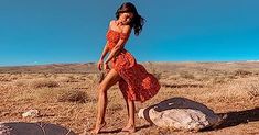 a woman in an orange dress is standing on some rocks