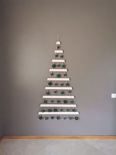 a white wooden christmas tree hanging on a gray wall with green glass ornaments around it