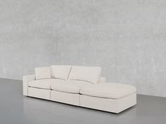 a white couch sitting on top of a floor next to a gray wall with no one in it