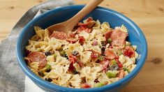 a blue bowl filled with pasta and meat on top of a wooden table next to a napkin