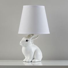 a white rabbit lamp sitting on top of a table next to a gray wall with a white shade