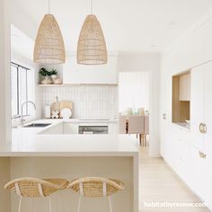 two wicker stools sit at the bar in this modern white and beige kitchen