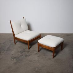 two wooden chairs with white cushions sit on concrete flooring in front of a wall