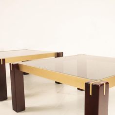 two tables with glass top and wooden legs on the floor in front of a white wall