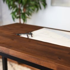 a wooden table with a pen and paper on it next to a potted plant