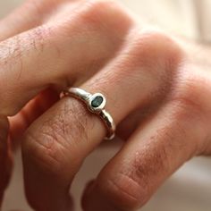 a close up of a person's hand wearing a silver ring with an emerald stone