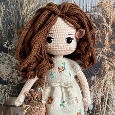 a crocheted doll with brown hair holding a basket in front of a painting