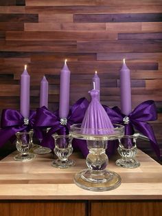 purple candles are sitting on top of a glass cake plate with satin ribbons around them