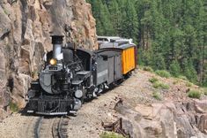 a train traveling down tracks next to a rocky hillside