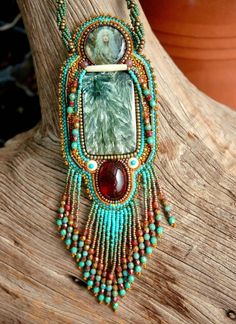 a necklace made with beads and stones on top of a wooden tree branch in front of a potted plant