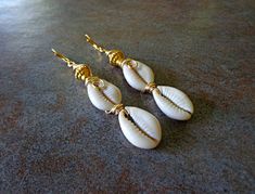 "Sea Shell Earrings, Beach Jewelry, Triple Cowrie Shell Earrings, Cowry Shells, Ethnic Dangle Earrings, African Earrings Double Cowrie Shell Dangle Earrings should definitely be in your jewelry wardrobe. This three row tier aligns perfectly well with the boldness of of gold to compliment, Approx 3.5\" length, copper ear wires. Cowrie shells were the most popular currency within Africa. Pictures of cowrie shells adorned cave walls. The Egyptians considered them to be magical agents and also used Traditional Nickel-free Earrings For Beach, Bohemian White Wire Wrapped Earrings, White Wire Wrapped Bohemian Earrings, White Bohemian Wire Wrapped Earrings, Africa Pictures, Cowrie Shell Earrings, Sea Shell Earrings, Cowry Shell, Earrings Beach