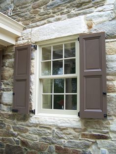 a stone building with two windows and brown shutters