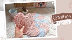 a hand holding a heart shaped pillow on top of a bed next to a cup