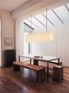 a dining room table and benches in front of a window with a skylight hanging from the ceiling