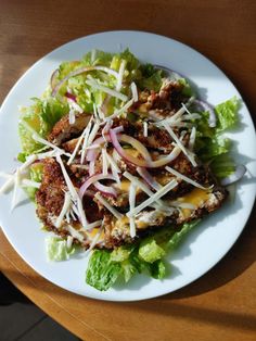 a white plate topped with lettuce and meat on top of a wooden table