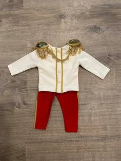 a baby's white and red outfit with gold trimmings on the chest