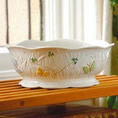 a white glass bowl sitting on top of a wooden shelf next to a potted plant