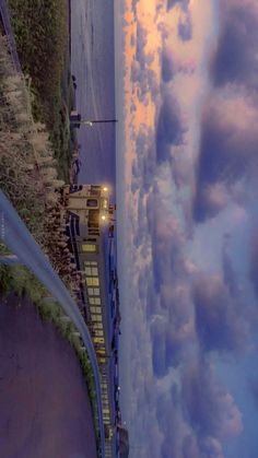 a train traveling down tracks next to the ocean at dusk with clouds in the sky