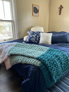 a bed with blue and white blankets on it in a bedroom next to a window