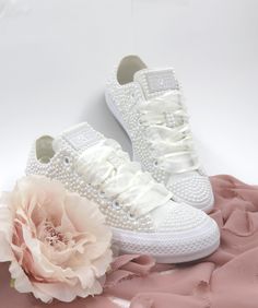 a pair of white sneakers with pearls on them and a flower laying next to it