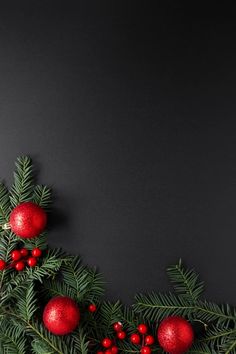 christmas tree branches with red ornaments on them against a black background, copy space for text