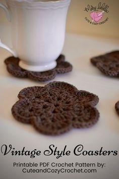 four crocheted coasters on a table next to a white cup and saucer