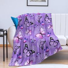 a purple blanket with pink butterflies on it sitting on a white couch in a living room