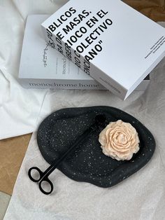 a pair of scissors sitting on top of a black plate next to a box with a rose in it