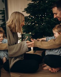 a man and woman holding a small child in front of a christmas tree while sitting on the floor