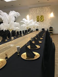 a long table with black and gold place settings, white feather centerpieces on each plate