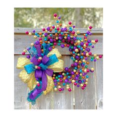 a purple and blue wreath with beads on it hanging from a wooden fence in front of some trees