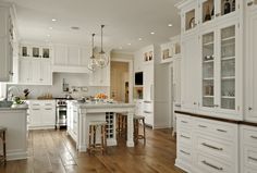 a large kitchen with white cabinets and wooden floors is pictured in this image, there are two stools at the center of the island