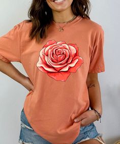 Elevate your wardrobe with this stunning vintage floral shirt featuring a bold, retro-inspired red rose graphic. Perfect for those who love the charm of cottagecore fashion and botanical prints, this flower t-shirt effortlessly combines style and comfort. Whether you're looking for a casual outfit or a unique gift for her, this floral aesthetic shirt is a perfect choice. Made from soft, high-quality fabric, this botanical tee is designed for all-day comfort and durability. The vibrant red rose design adds a pop of color, making it a standout piece in any collection. Whether you're dressing up for a day out in the garden or embracing your inner nature lover, this floral graphic tee is sure to become a favorite. Key Features: Premium Quality: Crafted from breathable, soft fabric that's perfe Summer Graphic Tee With Rose Print, Trendy Rose Print T-shirt For Spring, Rose Print Tops For Summer, Spring Graphic Tee With Rose Print, Spring Rose Print Graphic Tee, Spring Rose Print Short Sleeve T-shirt, Summer Rose Print Short Sleeve T-shirt, Summer Short Sleeve T-shirt With Rose Print, Spring Cotton T-shirt With Rose Print