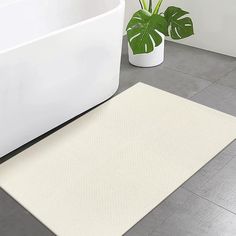 a white bath tub sitting next to a plant on top of a tiled bathroom floor