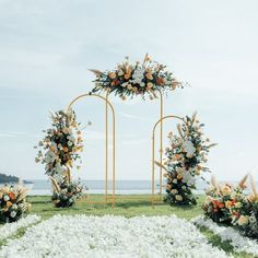 an outdoor ceremony setup with flowers and greenery on the grass, along with two archways