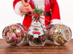 a santa clause standing next to three glass jars filled with christmas treats