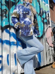 a woman standing in front of a wall with graffiti on it and wearing blue jeans