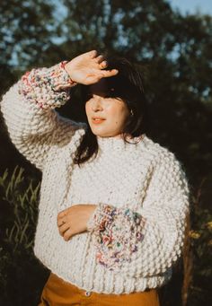 a woman in a white sweater and brown pants is holding her hand up to her head