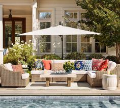 an outdoor living area next to a swimming pool with patio furniture and umbrella over it